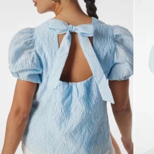 Ljusblå topp med puffärm och rosett från Vero Moda - Supersöt ljusblå topp från Vero Moda med puffiga korta ärmar och öppen rygg med stor rosett. Aldrig använd och prislappen sitter kvar, i storlek S. Nypris 600