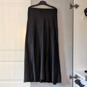 Svart satinkjol - En svart långkjol i satin med lätt glansig finish. Kjolen har en enkel och stilren design utan synliga detaljer och faller snyggt längs benen. Perfekt för dig som gillar minimalistisk stil.