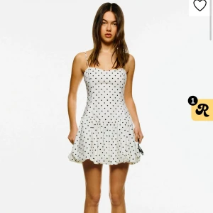 Vit prickig kortklänning med volang - Supersöt vit kortklänning med svarta prickar och volang nertill. Klänningen har smala axelband och en figurnära passform upptill som blir lite utsvängd nedtill. Perfekt för sommarens alla tillfällen!