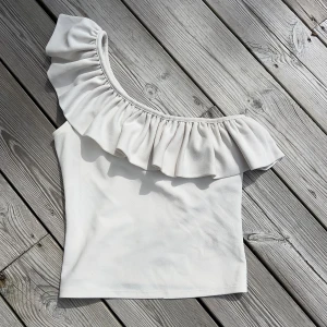 Vit oneshoulder topp med volang - Säljer en vit oneshoulder topp med volang. Jättefint till sommaren.🌺Skriv privat vid funderingar🤗
