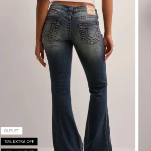 Blå bootcut jeans från True Religion - Snygga blå jeans från True Religion med bootcut-passform och klassiska kontrastsömmar. Jeansen har fem fickor, låg midja och ikoniska broderade bakfickor. Perfekta för en avslappnad och trendig look.