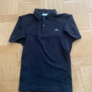 Svart Lacoste piké - Säljer en svart Lacoste piké i storlek S. Den är i mycket bra skick och inga som helst defekter. Hör av er vid frågor