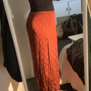 Röd långkjol från Indiska - Säljer en vacker röd långkjol från Indiska med subtilt blommigt mönster❣️Kjolen har hög midja och en slit. Sedan stängs den med dragkedja och två knappar framtill:) Skriv om frågor finns! 