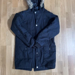 Svart parkajacka med fuskpäls från Pepperts! Teens - Svart parkajacka med huva och fuskpäls från Pepperts! Teens. Jackan har långa ärmar, stora fickor framtill med knappar och dragkedja samt knäppning framtill. Perfekt för kyliga dagar.