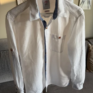 S.Oliver vit herr linneskjorta i nyskick. S - •Vit skjorta med lång ärm från S.Oliver.  •Skjortan har en bröstficka och knappar i träimitation. •Detaljer i blått vid krage och ärmslut. •Knappt använd, nyskick. Tvättad.  •Djurfritt och rökfritt hem. 