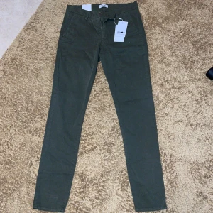 Olivgröna chinos från NN07 - Säljer ett par olivgröna chinos från NN07 med klassisk passform. Byxorna har dragkedja, knappstängning och två bakfickor med knappar. Perfekta för en stilren och avslappnad look. Aldrig använt, bara legat i garderoben. (Nypris 1299kr). Pris kan diskuteras😉