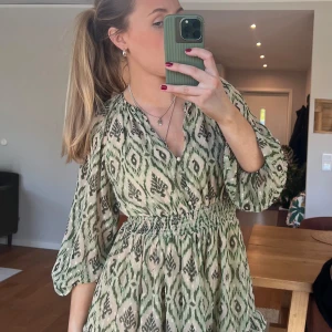 Grön mönstrad kortklänning med volang - Säljer en grön och beige kortklänning med mönster och volangdetaljer.🤍