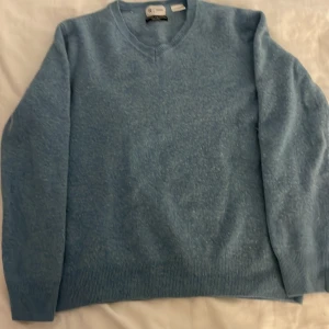 Ljusblå merinoullströja från La Redoute - Säljer en ljusblå tröja i mjuk merinoull och kashmir från La Redoute. Tröjan har v-ringad hals, långa ärmar och ribbade muddar vid ärmslut och nederkant. Perfekt för lager-på-lager och stilren look.