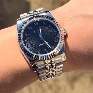 Seiko automatisk klocka med blå urtavla - Snygg Seiko automatisk klocka med blå urtavla och arabiska siffror. Boett och länk i silverfärgat stål med räfflad bezel. Klassisk design som passar till många tillfällen.