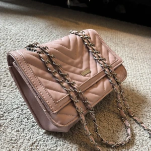 Rosa quiltad axelväska från Don Donna - Säljer en snygg rosa axelväska från Don Donna med quiltat mönster och kedjerem. Väskan har ett fack med lock och en dragkedja på baksidan. Perfekt accessoar för att lyfta din outfit!