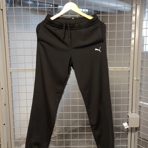Svarta träningsbyxor från Puma - Svarta träningsbyxor från Puma med dragsko i midjan och klassisk logga på låret. Byxorna har en normal passform och är tillverkade i ett syntetmaterial som passar perfekt för träning.