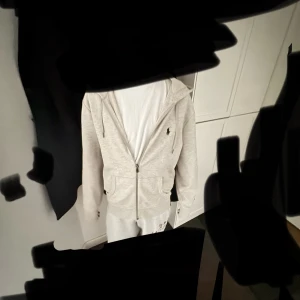 Grå hoodie med dragkedja från Polo raulph lauren - Säljer en stilren ljusgrå hoodie från Ralph Lauren med dragkedja framtill och huva. Hoodien är knappt använd med inga hål eller fläckar. Tröjan har två fickor och en liten broderad logga på bröstet. Perfekt för en avslappnad look. Pris kan diskuteras och skriv för mer bilder. 