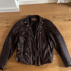 Brun skinnjacka från Jofama - Säljer en brun skinnjacka från Jofama med klassisk bikerstil. Jackan har dragkedjor, axelklaffar och spännen i sidorna. Snygga detaljer och flera fickor framtill. Perfekt för dig som gillar tidlös stil och vill sticka ut.