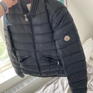 Svart pufferjacka från Moncler - Säljer en svart pufferjacka från Moncler med dragkedja framtill och två snedställda fickor med dragkedja. Jackan har lång ärm och Moncler-logga på ena ärmen. Perfekt för kyligare dagar.  Storlek 3