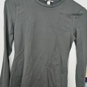 Mörkgrå långärmad tröja - En enkel och stilren mörkgrå långärmad tröja med rund halsringning från H&M med etiketten på. Perfekt basplagg som funkar till det mesta och är lätt att matcha med andra kläder. Mjuk och skön mot huden.