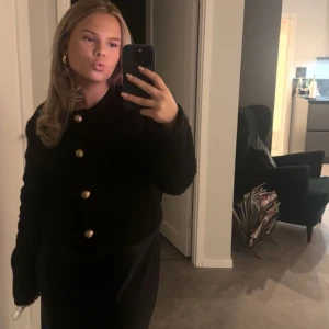 Svart cardigan jacka med guldknappar - Säljer en svart cardigan jacka med stora guldknappar framtill. Jackan har lång ärm och en klassisk, rak passform. Perfekt för dig som vill ha en stilren och enkel look.