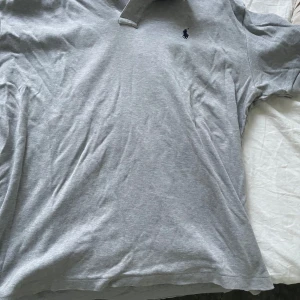 Grå pikétröja från Polo Ralph Lauren - Klassisk grå pikétröja från Polo Ralph Lauren med broderad marinblå logga på bröstet. Tröjan har krage och korta ärmar, perfekt för en stilren och avslappnad look. kom gärna med prisförslag 😊