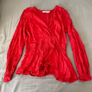 Röd omlottblus från NA-KD - Säljer en röd omlottblus från NA-KD med långa ärmar och markerad midja. Blusen har volangdetaljer nertill och en v-ringad omlottfront. Perfekt för dig som vill ha en färgstark och trendig topp! Säljer då den är förstor för mig!💕