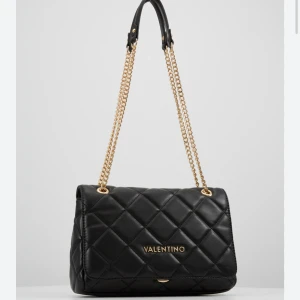 Valentino väska  - Svart axelväska från Valentino med quiltad design och guldfärgade kedjehandtag. Perfekt för att ge en lyxig touch till din outfit.                  Skriv gärna för egna bilder☺️