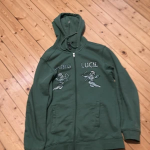 Grön hoodie från Blinglucid - Snygg grön hoodie från Blinglucid med dragkedja och huva. Den har coola detaljer med text och motiv på framsidan. Perfekt för en avslappnad stil. Kan gå ner i pris