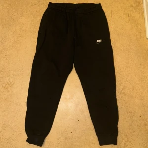 Svarta mjukisbyxor från Nike - Säljer ett par svarta mjukisbyxor från Nike. Byxorna har en elastisk midja och muddar vid bensluten för en bekväm passform. Perfekta för en avslappnad stil.