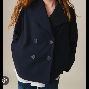 Svart kappa med knappar - Snygg svart kappa med dubbelknäppning och bred krage. Perfekt för kyligare dagar och ger en stilren look. Passar bra till både jeans och klänning.