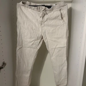 Beige linnebyxor - Säljer ett par bekväma beige linnebyxor med elastisk midja. Perfekta för en avslappnad stil. Byxorna har en enkel design utan mönster eller extra detaljer.