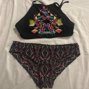 Mönstrad bikini från Gina - Snygg bikini från gina med färgglatt geometriskt mönster i rosa, blått och gult på svart bakgrund. Toppen har smala axelband och en hög halsringning. Perfekt för sommarens badäventyr!
