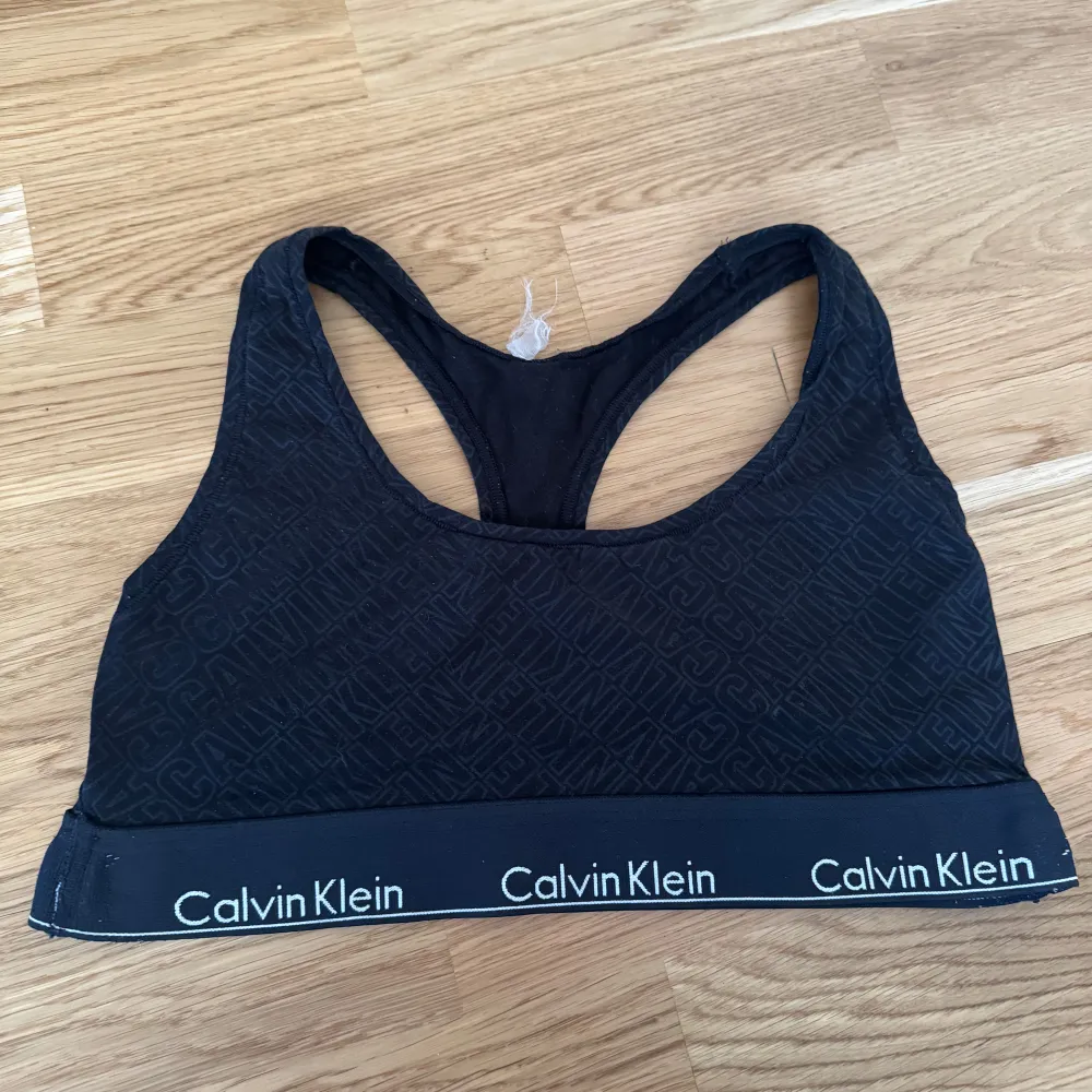 Säljer en svart sporttopp från Calvin Klein med ett diskret mönster och elastiskt band med logotyp. Perfekt för träning eller en avslappnad look. Toppen är ärmlös och har en bekväm passform.. Yläosat.
