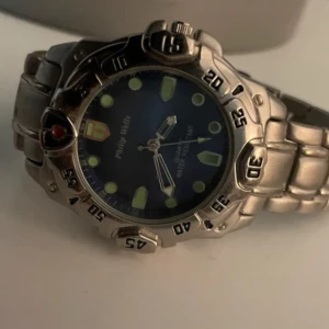 Helt ny Silverfärgad klocka från Philip Wells - Helt ny o Snygg och robust klocka från Philip Wells med en silverfärgad stål/metallarmband och blå urtavla. Klockan har tydliga markeringar och en vridbar bezel. Perfekt för den som gillar en sportig stil. Vattentät. 