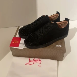 Svarta Louboutins med nitar - Svarta Louboutin med nitar på tån. Skorna har en klassisk design med snörning och en röd sula som ger en ikonisk touch. Skorna är i storlek 44 men passar även 45. Skorna är aldrig använda.
