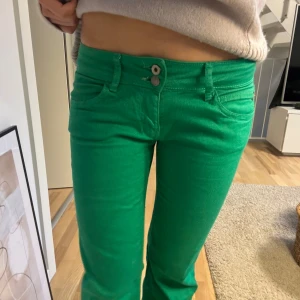 Gröna byxor low waist - Snygga gröna byxor från Indiwalles med låg midja och bootcut-stil. Byxorna har två knappar och dragkedja framtill. Perfekta för en färgglad look!