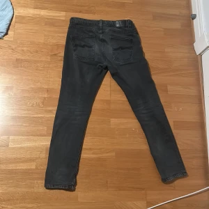 Svarta jeans från Nudie Jeans. Grim Tim - Säljer ett par svarta jeans från Nudie Jeans. De har en klassisk femficksdesign och knappar i gylfen. Har desvärre fått ett hål i vänstra ficka. 