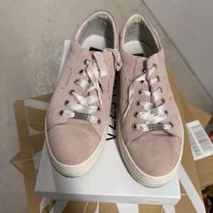 Rosa sneakers från Ella of Sweden - Snygga rosa sneakers från Ella med vita snören och dekorativa nitar på baksidan. Skorna har en rund tå och är tillverkade i mocka. Perfekta för en stilren look.