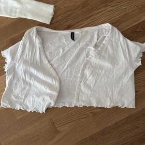 Vit bolerotopp från H&M - Säljer en vit bolerotopp från H&M med korta ärmar och knappar framtill. Perfekt för att lägga till en extra touch till din outfit. 💫