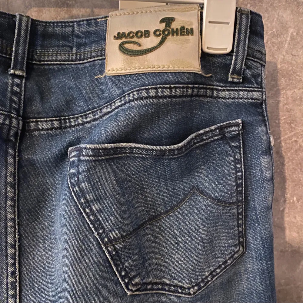 Snygga blå jeans från Jacob Cohen med knappgylf och klassisk femficksdesign. Jeansen har en stilren look med lätt slitna detaljer och en bekväm passform. Nypris 5000. Farkut & Housut.