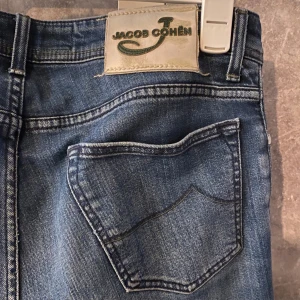 Blå jeans från Jacob Cohen - Snygga blå jeans från Jacob Cohen med knappgylf och klassisk femficksdesign. Jeansen har en stilren look med lätt slitna detaljer och en bekväm passform. Nypris 5000