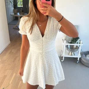 Vit kortklänning med knappar - Säljer en söt vit kortklänning med knappar framtill och v-ringad. Så fin till sommar/student💕 Finns inte längre att köpa!