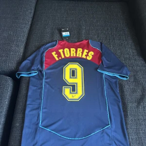 Blå fotbollströja med Spiderman-motiv - Säljer en unik blå fotbollströja från Nike med Spiderman-motiv och Atlético Madrid-logga. Tröjan har korta ärmar och ett coolt spindelnätsmönster på framsidan. På baksidan finns namnet F. Torres och nummer 9 i gult. Storlek m och en replika helt ny med tagg