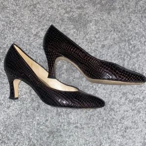 Brun svarta pumps från Naturalizer - Eleganta brun svarta pumps med krokodilpräglat mönster från Naturalizer. Skorna har en spetsig tå och en bekväm klack, perfekt för en stilren look.