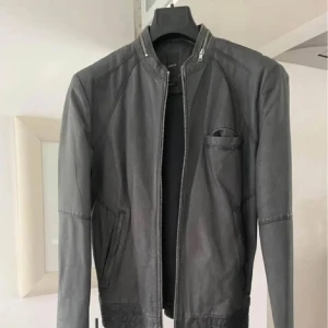 Grå äkta  skinnjacka från Emilio  - Snygg grå skinnjacka från Emilio i storlek S. Jackan har en stilren design med dragkedja framtill och flera praktiska fickor. Perfekt för en cool och avslappnad look. Äkta skinn, super fin grå färg. Oanvänd 