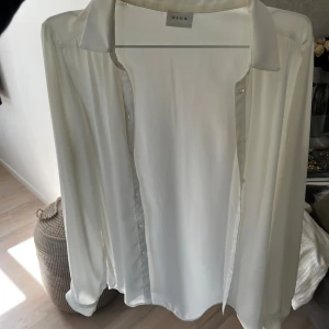 Vit blus från VILA - Elegant vit blus från VILA med klassisk krage och knappar framtill. Perfekt för en stilren look.