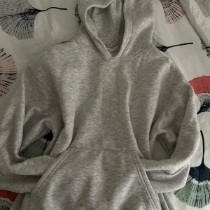 Grå hoodie från Ginatricot - Säljer en stilren grå hoodie från Ginatricot. Den har en klassisk design med en stor ficka framtill och en bekväm huva. Perfekt för en avslappnad look. Ribbstickade muddar vid ärmsluten ger en snygg passform. Passar sköna väder som vår och höst☺️