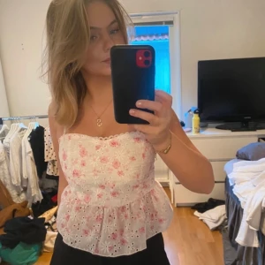 Vit blommig topp med spetsdetaljer - Somrig söt vit broderad bandeu topp med rosa blommönster och spetsdetaljer. Storlek S/M