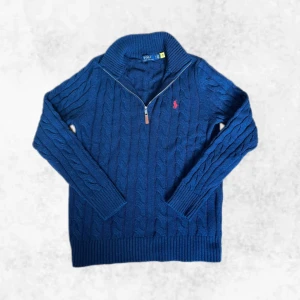 Marinblå kabelstickad half zip från Polo Ralph Lauren - Säljer en snygg marinblå kabelstickad half zip från Ralph Lauren med dragkedja och klassiskt kabelstickat mönster. Tröjan har en liten röd broderad logga på bröstet och ribbade muddar. Perfekt för kyliga dagar! Den är i nyskick, endast testad. Storlek M men kan även passa en större S. Vid några frågor eller funderingar är det bara att höra av sig.