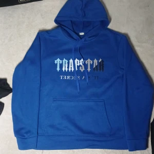 Blå hoodie från Trapstar - Säljer en blå hoodie från Trapstar med texten 'It's a Secret' på framsidan. Tröjan har en klassisk känguruficka och en bekväm huva. Perfekt för en avslappnad stil. Storleken S, jag är 180 och den sitter snyggt och slim på mig. Pris kan diskuteras.