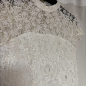 Vit spetsklänning från Ida Sjöstedt - Elegant vit spetsklänning från Ida Sjöstedt från NA-KD. Klänningen har korta ärmar och ett vackert blommönster med pärldetaljer. Perfekt för speciella tillfällen tex nu inför studenten.