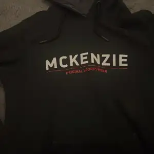 Säljer en svart hoodie från McKenzie med texten 'Original Sportswear' i vitt och rött på framsidan. Perfekt för en avslappnad stil. Den har en klassisk huva med dragsko.