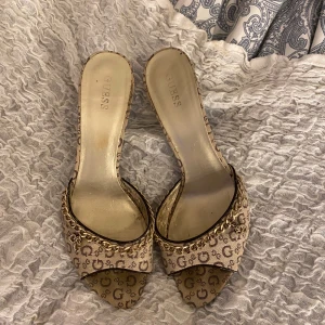 Klackar med kedjedetalj från Guess - Från Guess med ett ikoniskt mönster och guldfärgad kedjedetalj. har en öppen tå, storlek 40  klackhöjd ca 8 cm💞säljer för att dom e för stora för mig! Snabb köp och diskuterar gärna om priset