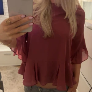 Vinröd blus med volang - Blusen har en lös passform och är tillverkad i ett tunt, lätt material som ger ett luftigt intryck från Vero Moda.